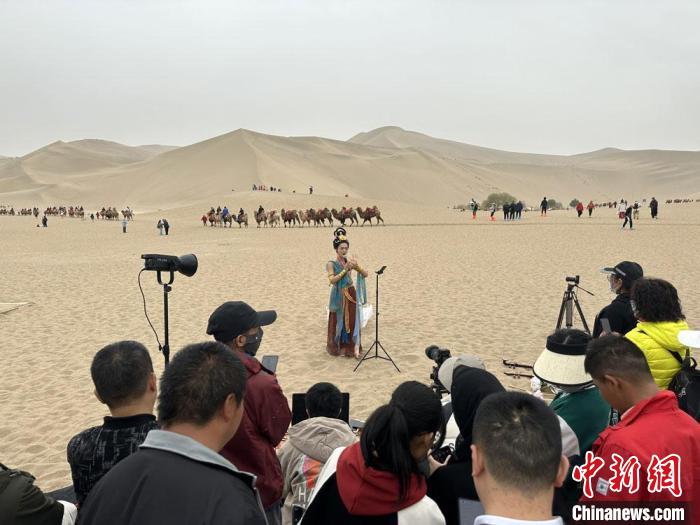 圖為2023年4月底，敦煌大漠“逐舞者”奧楠在鳴沙山月牙泉景區(qū)視頻直播，吸引游人圍觀?！●T志軍 攝
